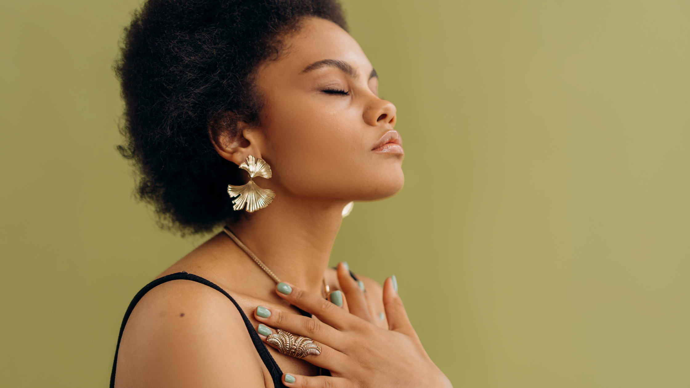 Black feminine presenting person with their hands pressed against their chest, eyes closed, meditating or praying.